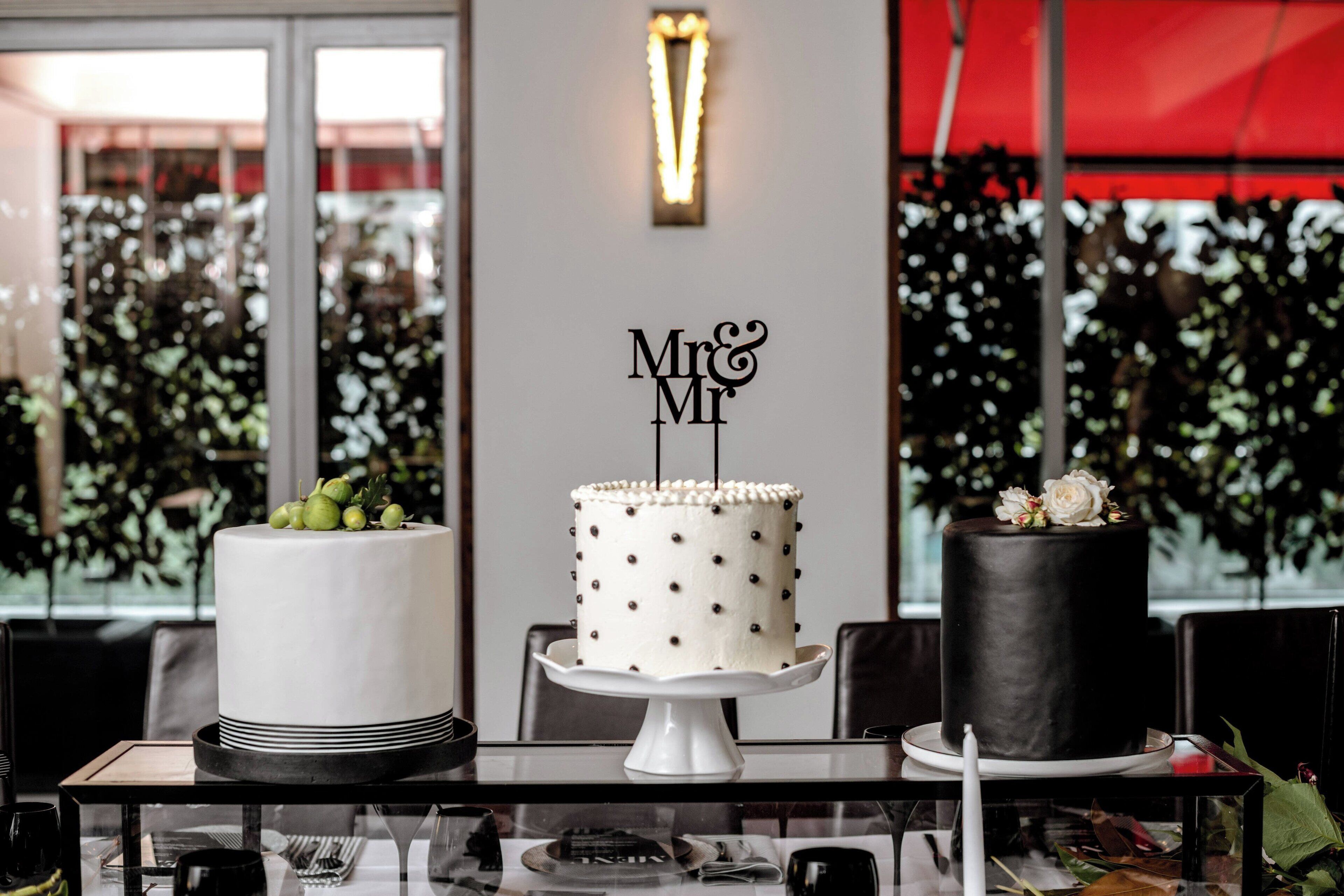 Una mesa con tres pasteles, cada uno decorado de manera distinta, en una habitación de diseño moderno y amplios ventanales.