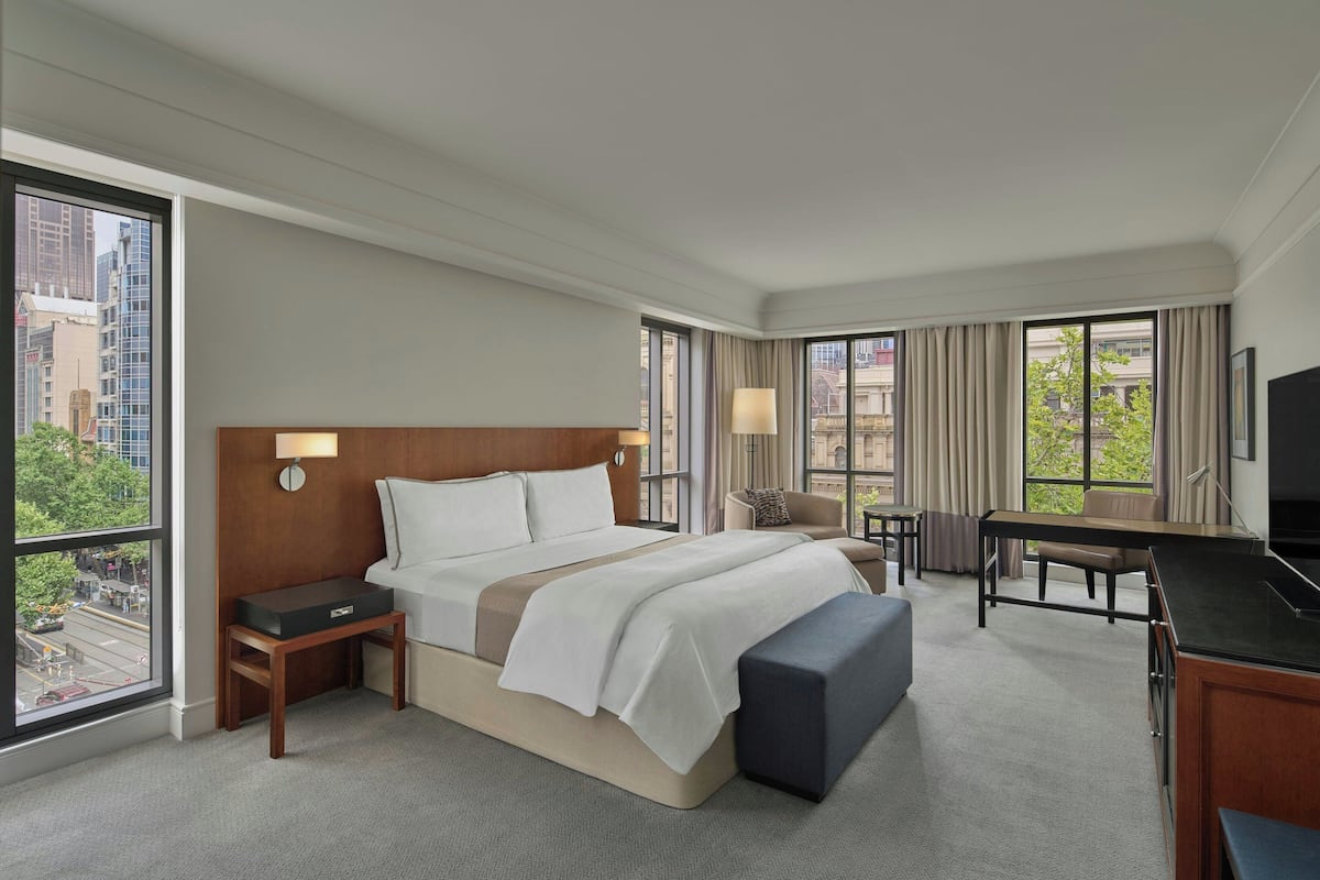 Habitación de hotel con una cama grande, un escritorio, una silla, un televisor y una ventana con vista a la ciudad.