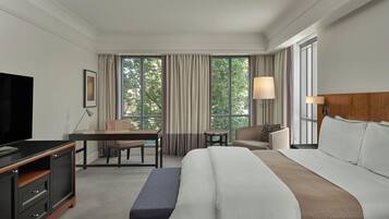 A hotel room with a large bed, a desk, a chair, a TV, and a window with curtains.