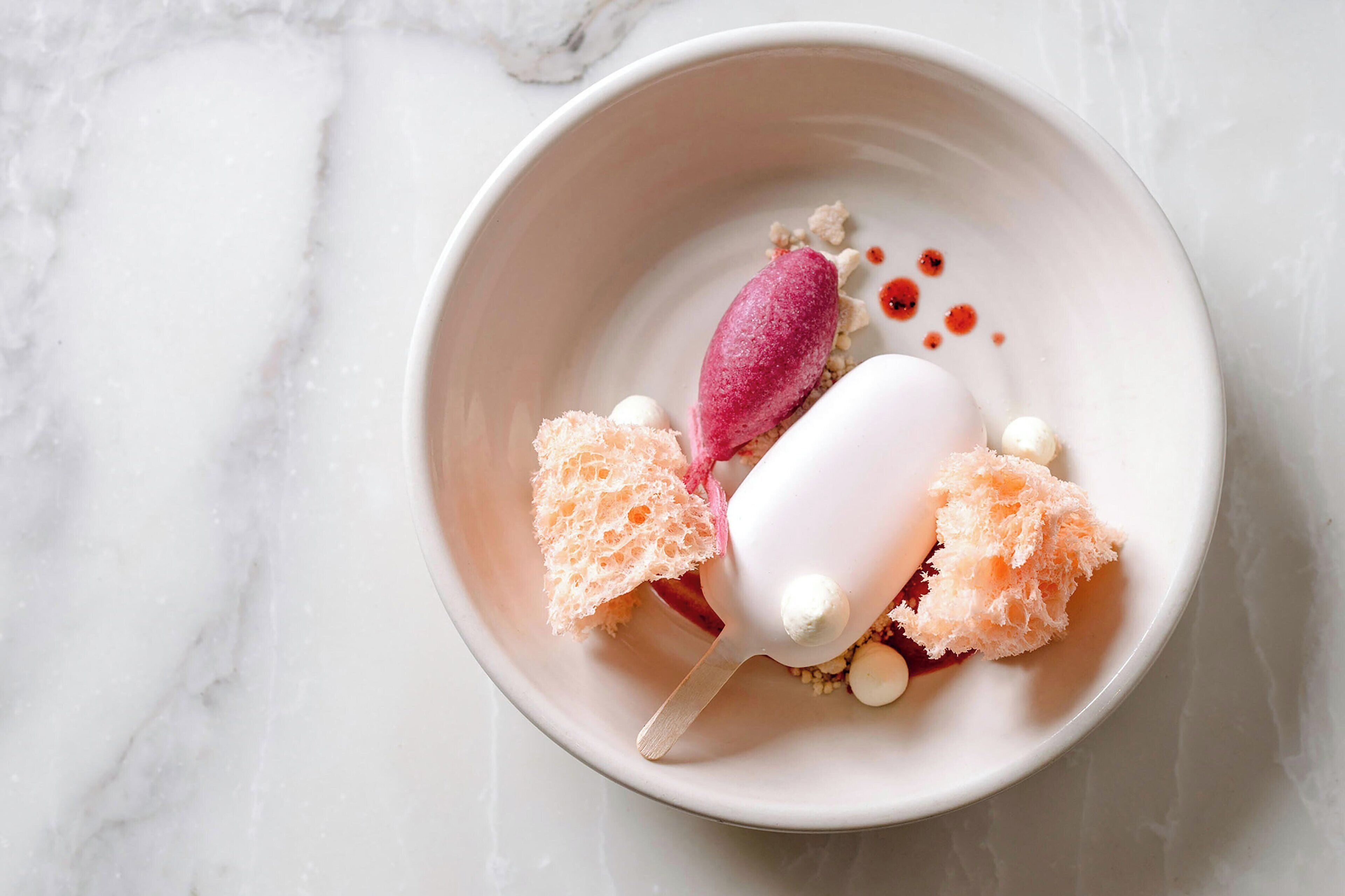 A dessert plate with a scoop of ice cream, two pieces of cake, and a spoon on a marble surface.
