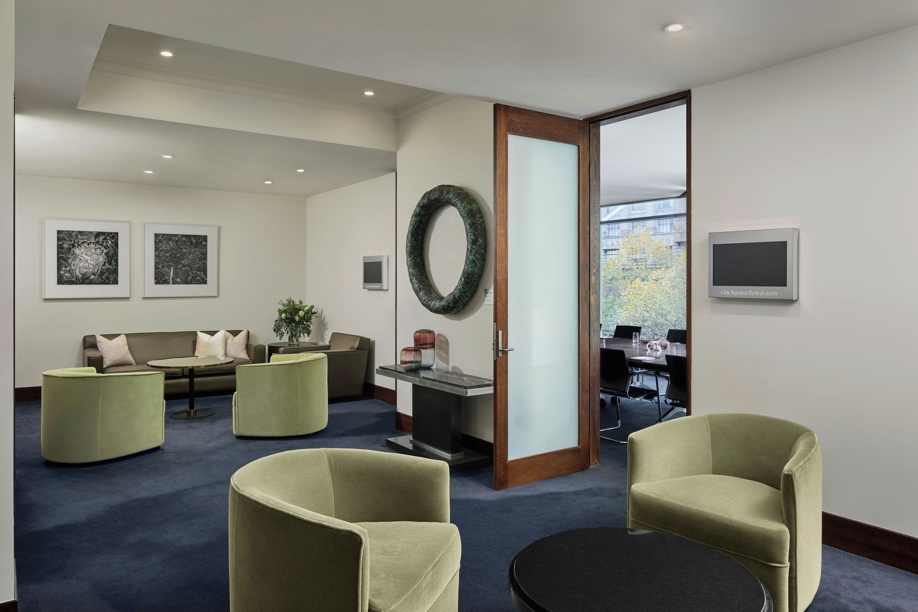 A modern hotel lobby with a seating area, a reception desk, and a large window.