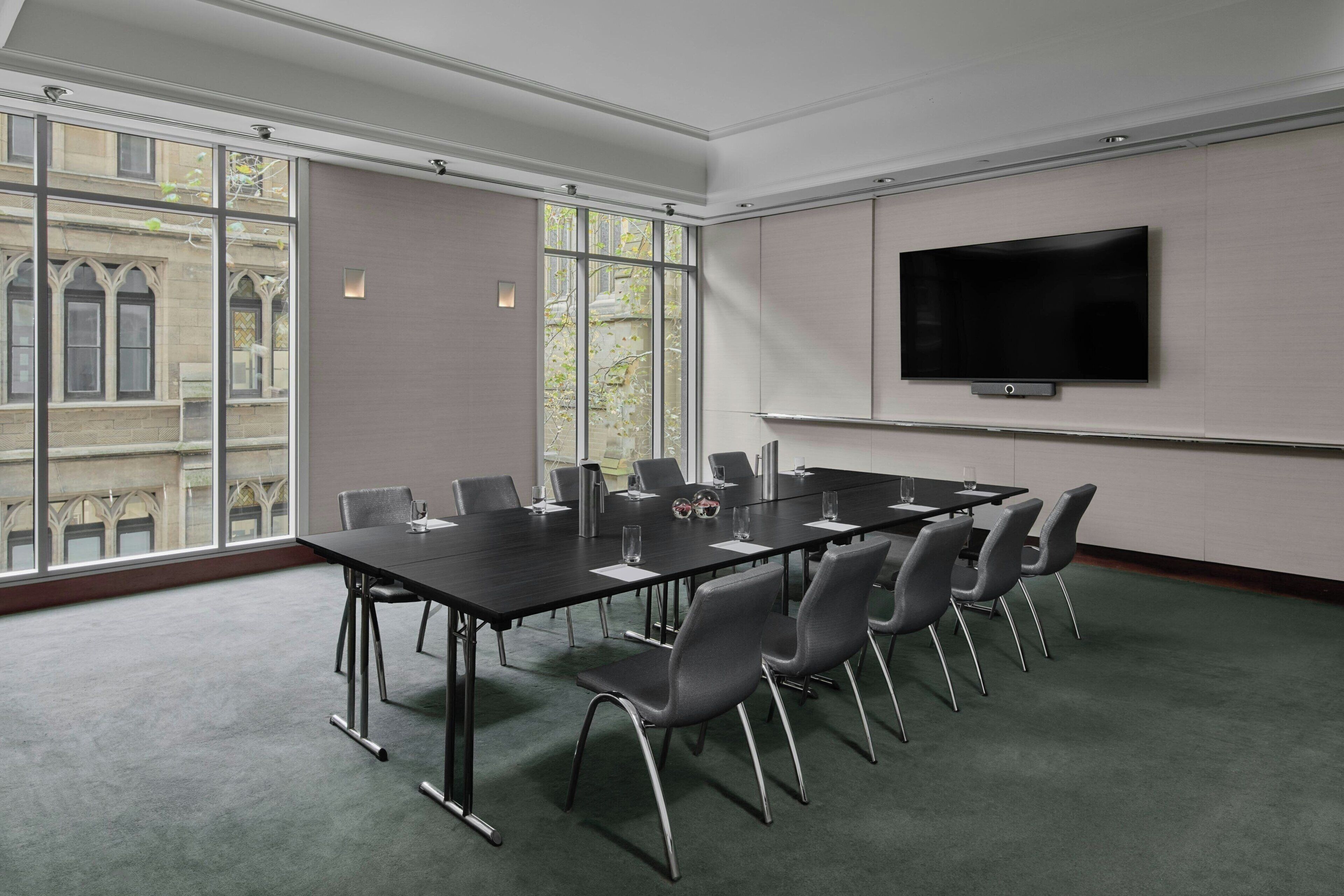 A conference room with a long table, chairs, a flat-screen TV, and large windows.