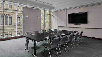 A conference room with a long table, chairs, a flat-screen TV, and large windows.