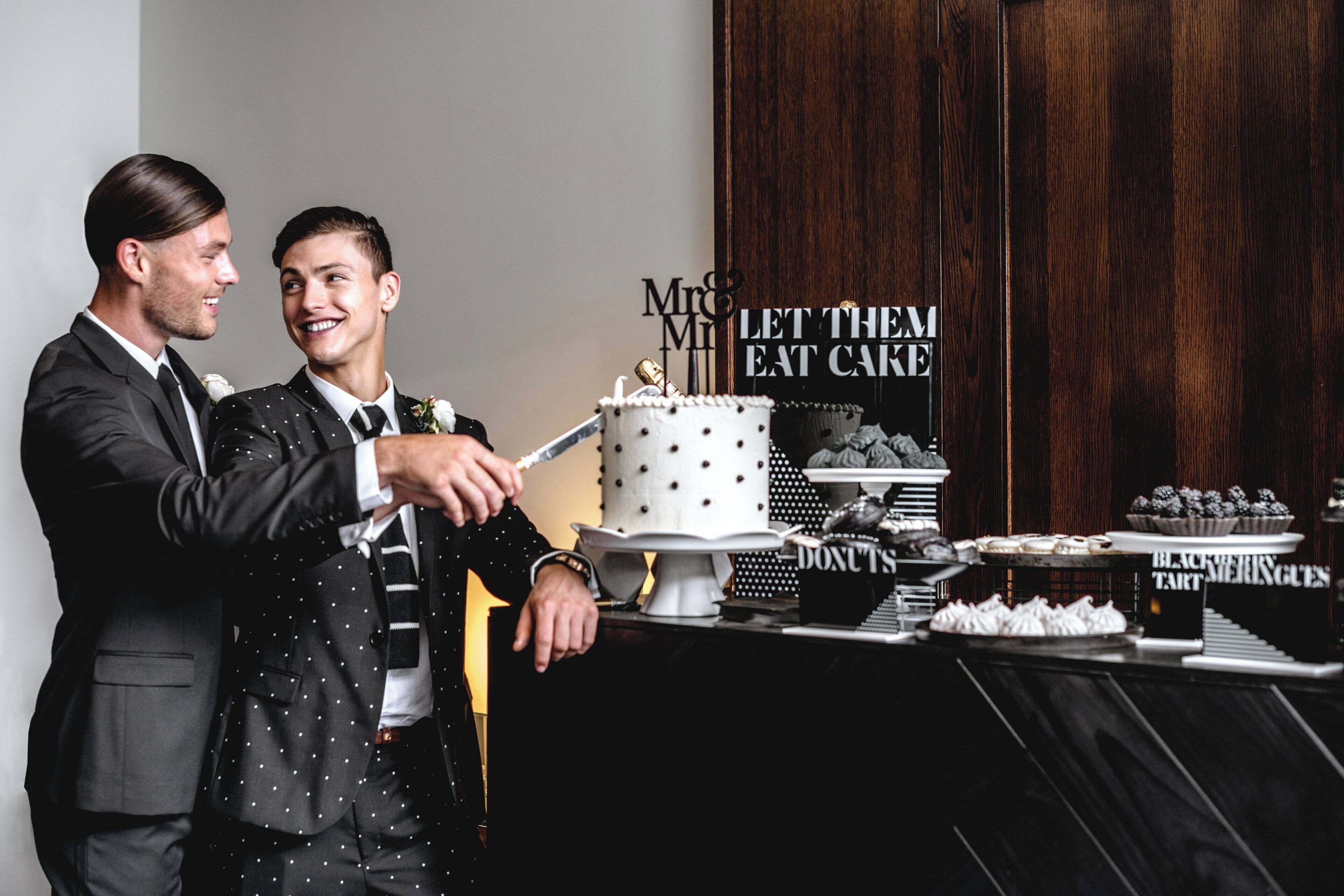 Two men in suits cutting a cake with a 'Mr & Mrs' topper.