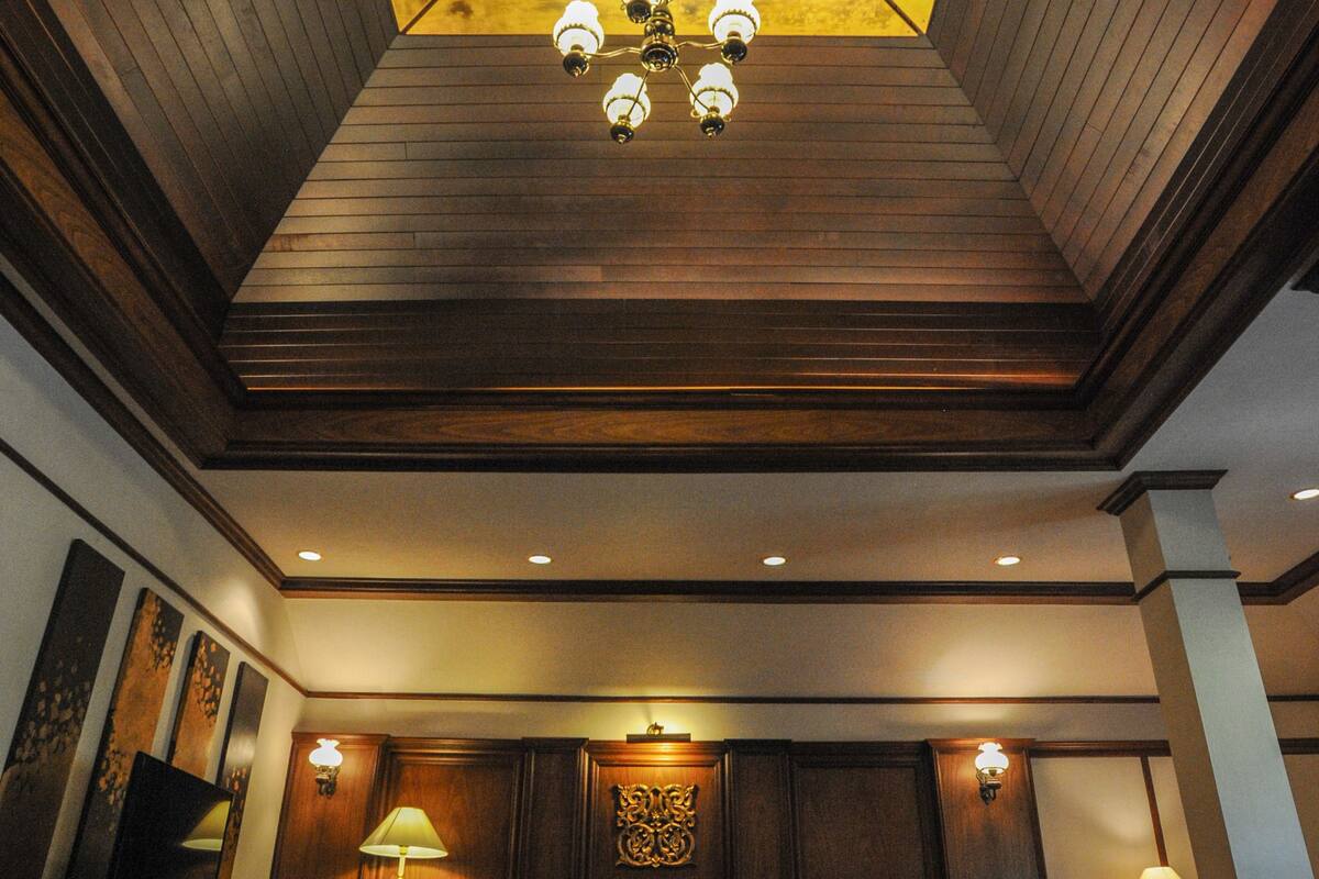 A room with a wooden ceiling, recessed lighting, and a chandelier. There are two sofas and a coffee table.