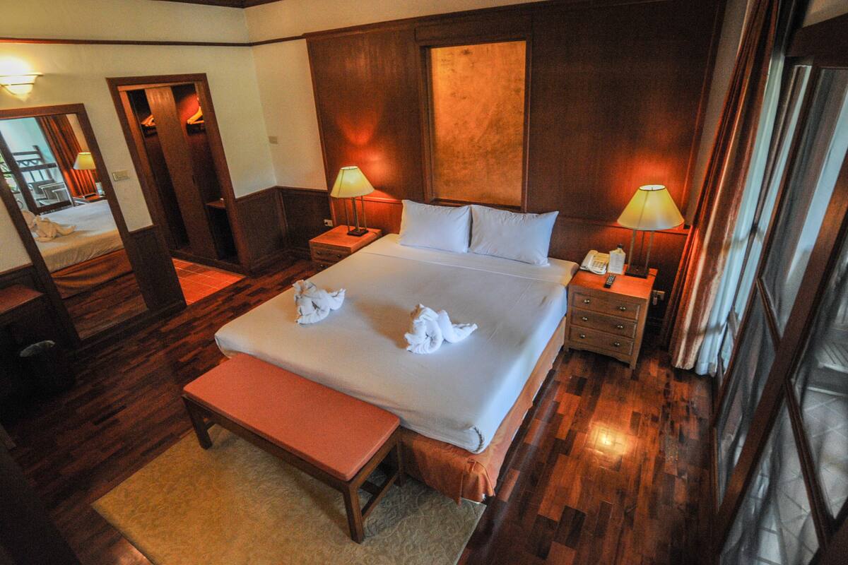 A hotel room with a large bed, two bedside tables with lamps, a bench, a mirror, and wooden flooring.