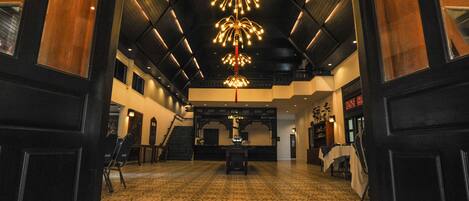 A spacious lobby with patterned flooring, a central chandelier, and a staircase leading to upper levels.