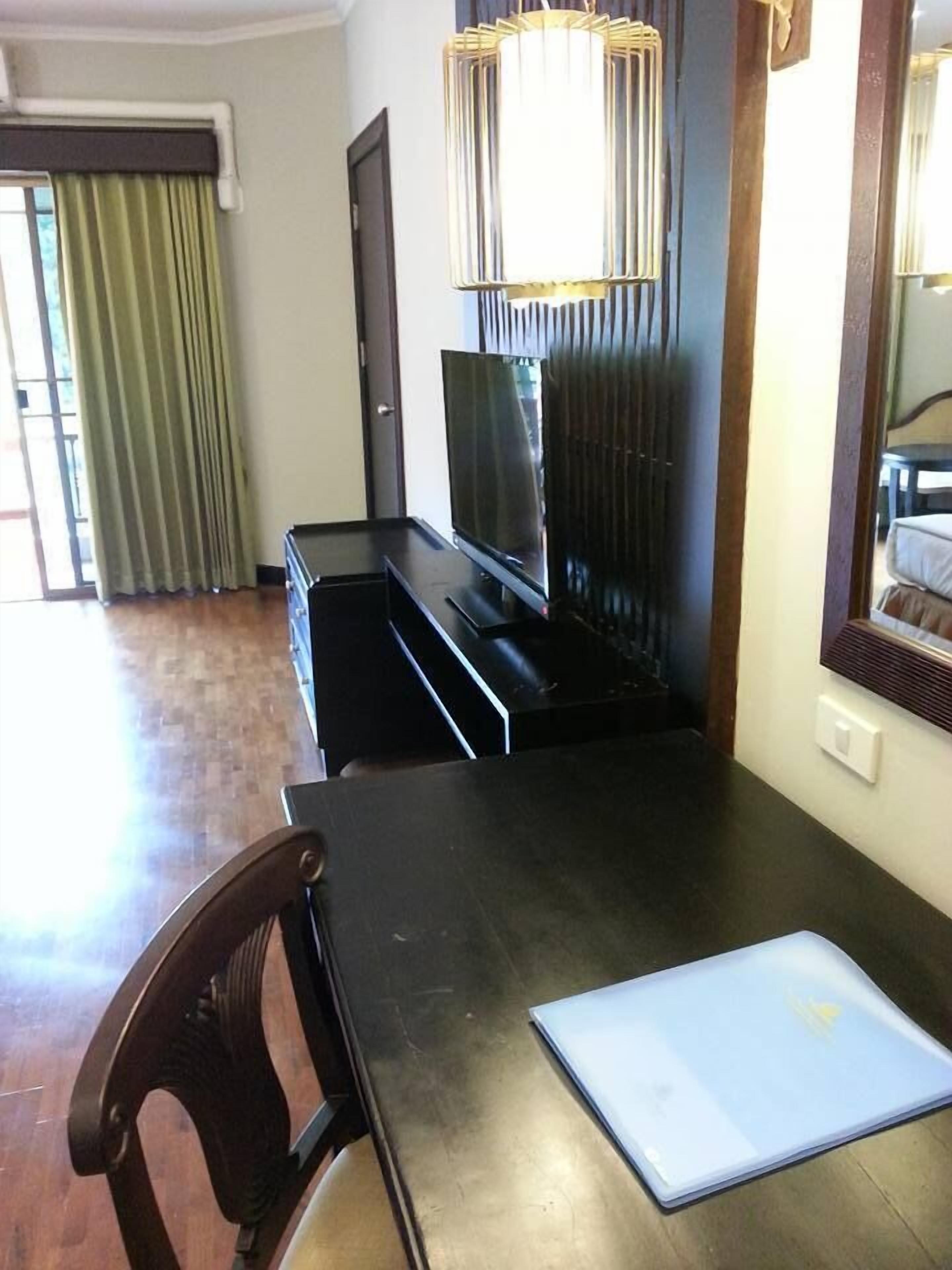 A modern hotel room with a dark wooden dining table, a laptop, and a television.