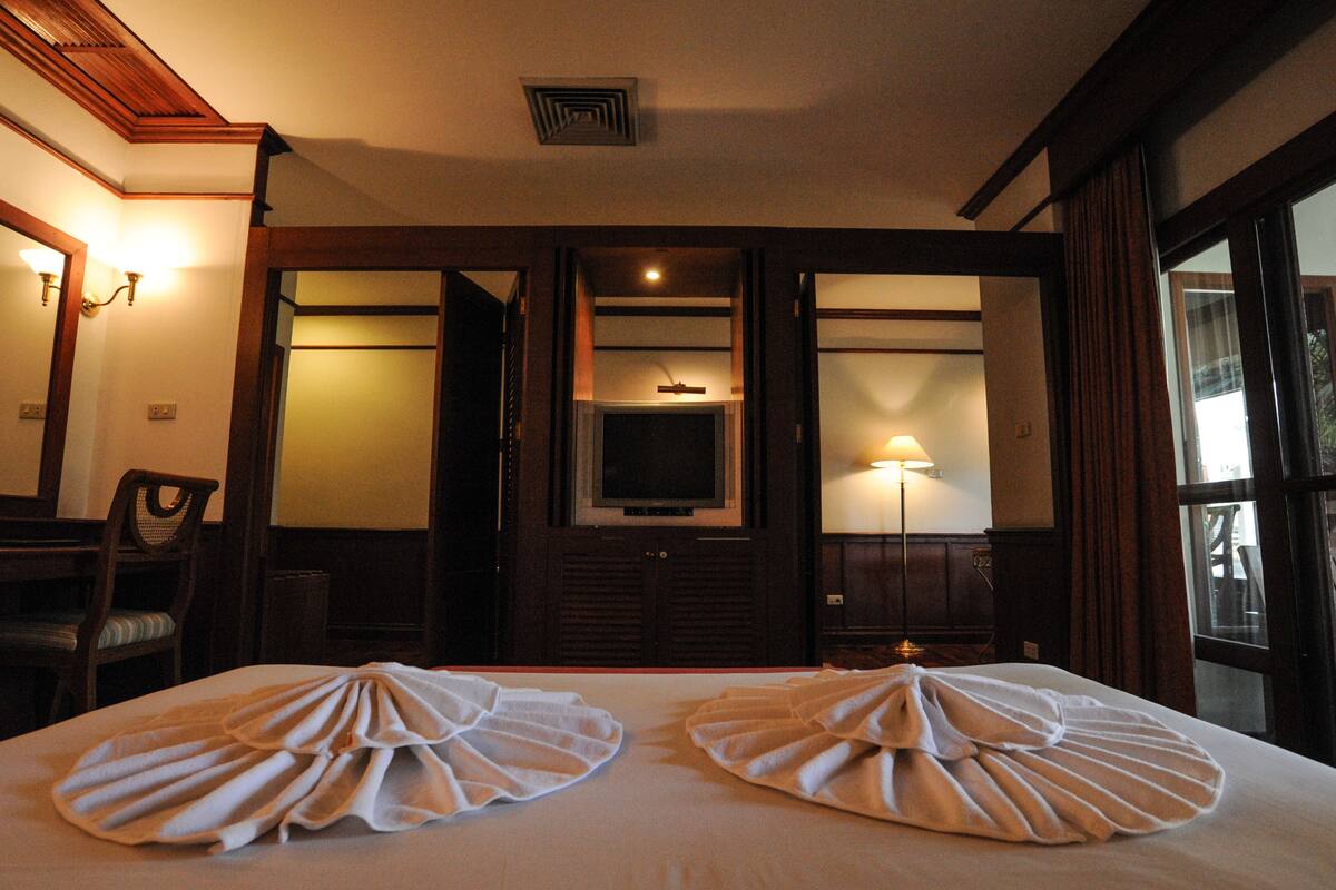 A hotel room with two beds, a television, a desk with a chair, and a window with curtains.