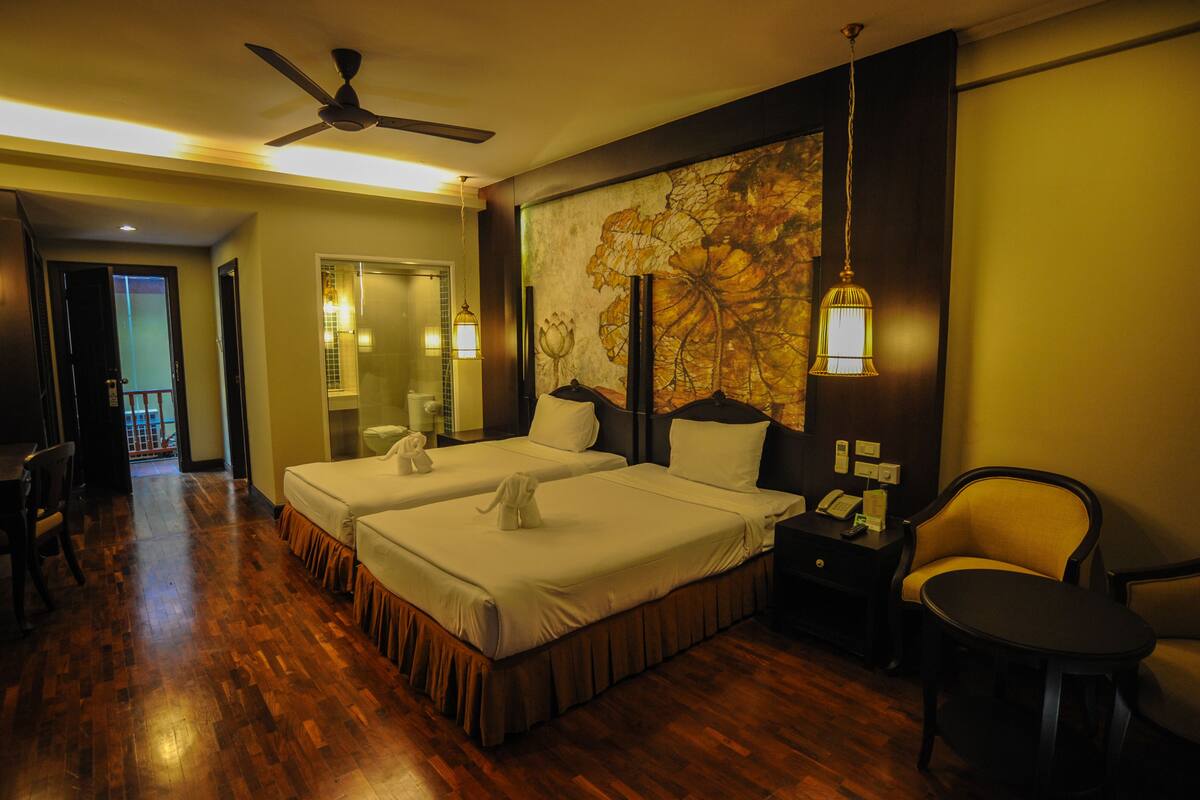 A hotel room with two beds, a ceiling fan, a large floral artwork on the wall, and a desk with a telephone.