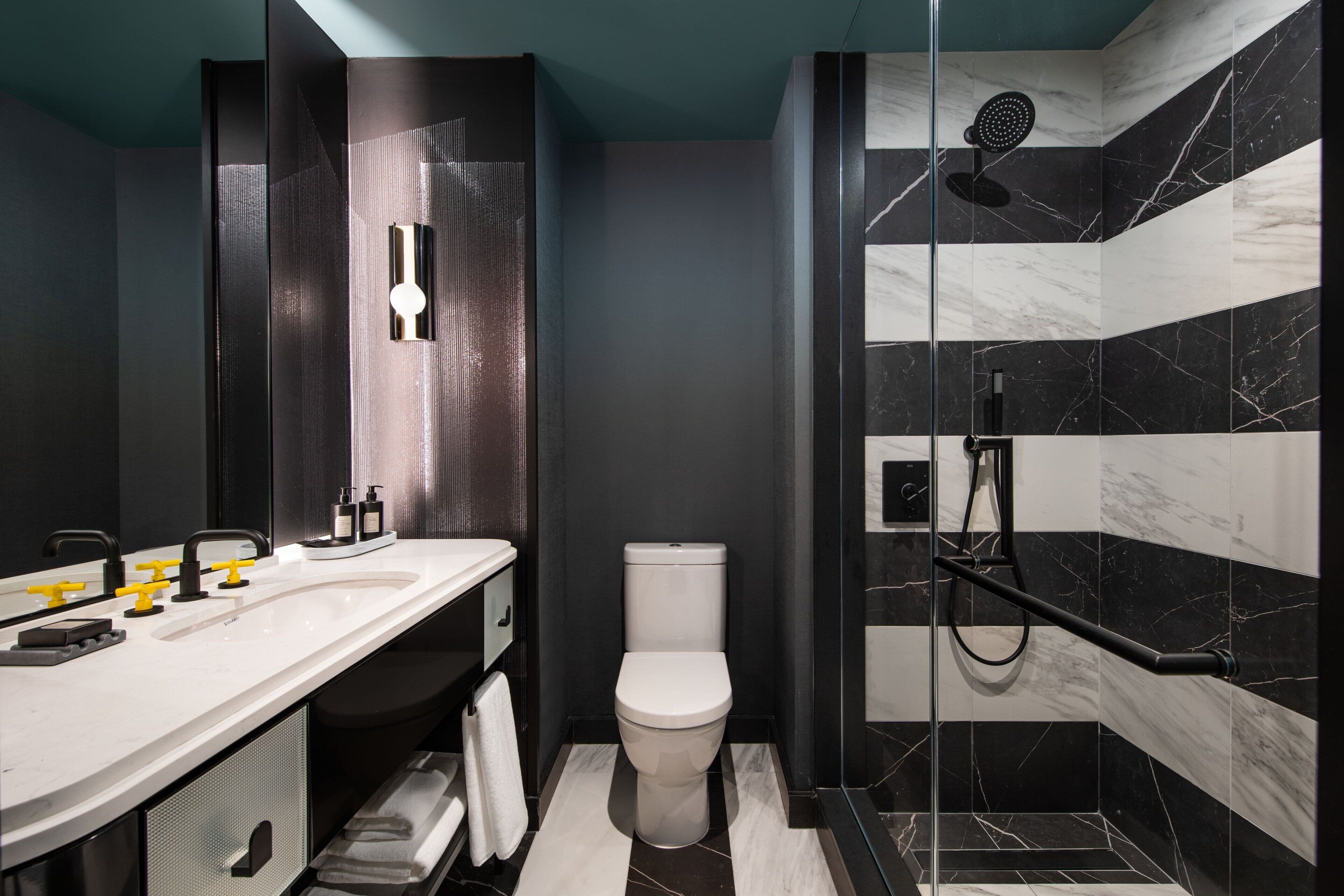 A modern bathroom with a large mirror, a white sink with yellow faucets, a toilet, and a glass-enclosed shower area.