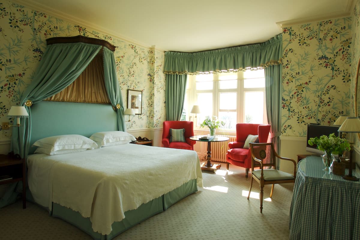 A bedroom with a large bed, a red armchair, a small table, and a television.