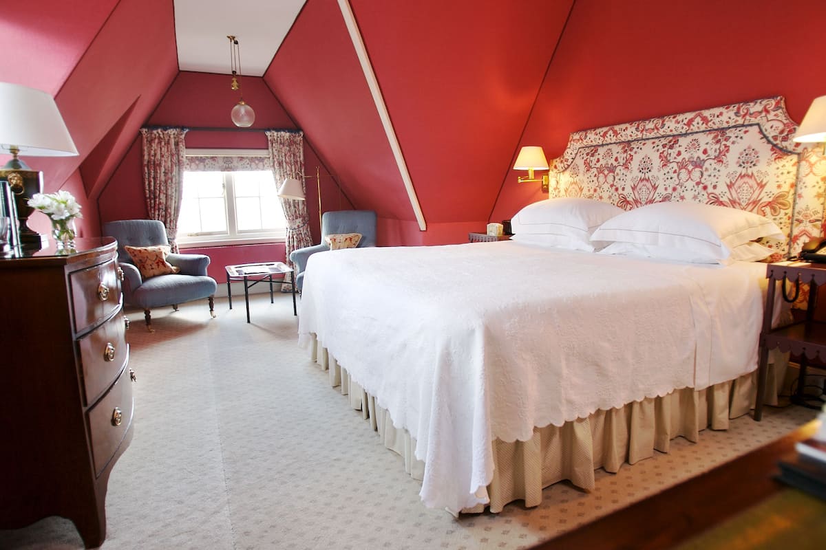 A bedroom with a large bed, a dresser, a chair, and a window with curtains.