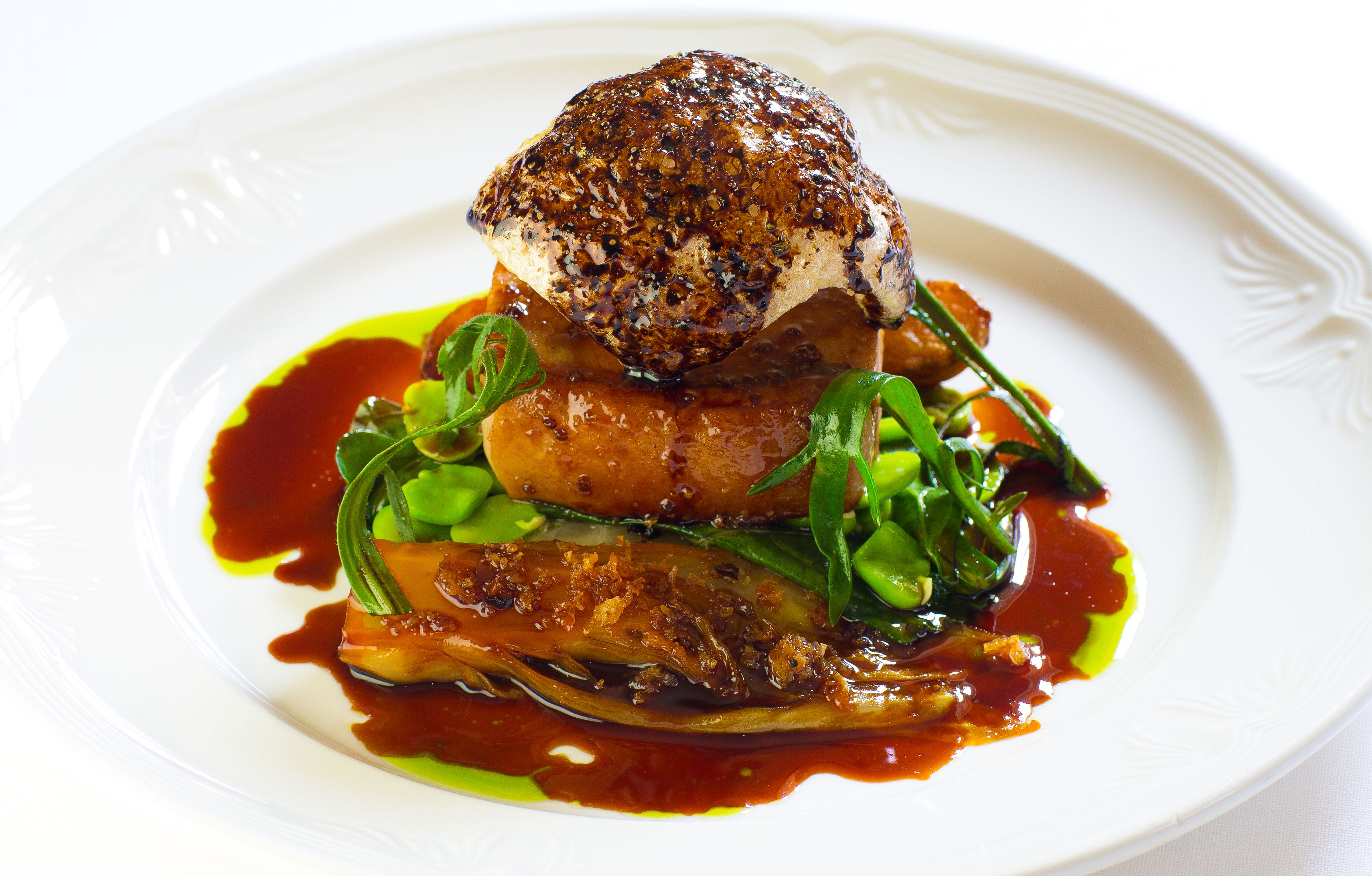 A white plate with a dish consisting of a seared fish, greens, and a sauce.