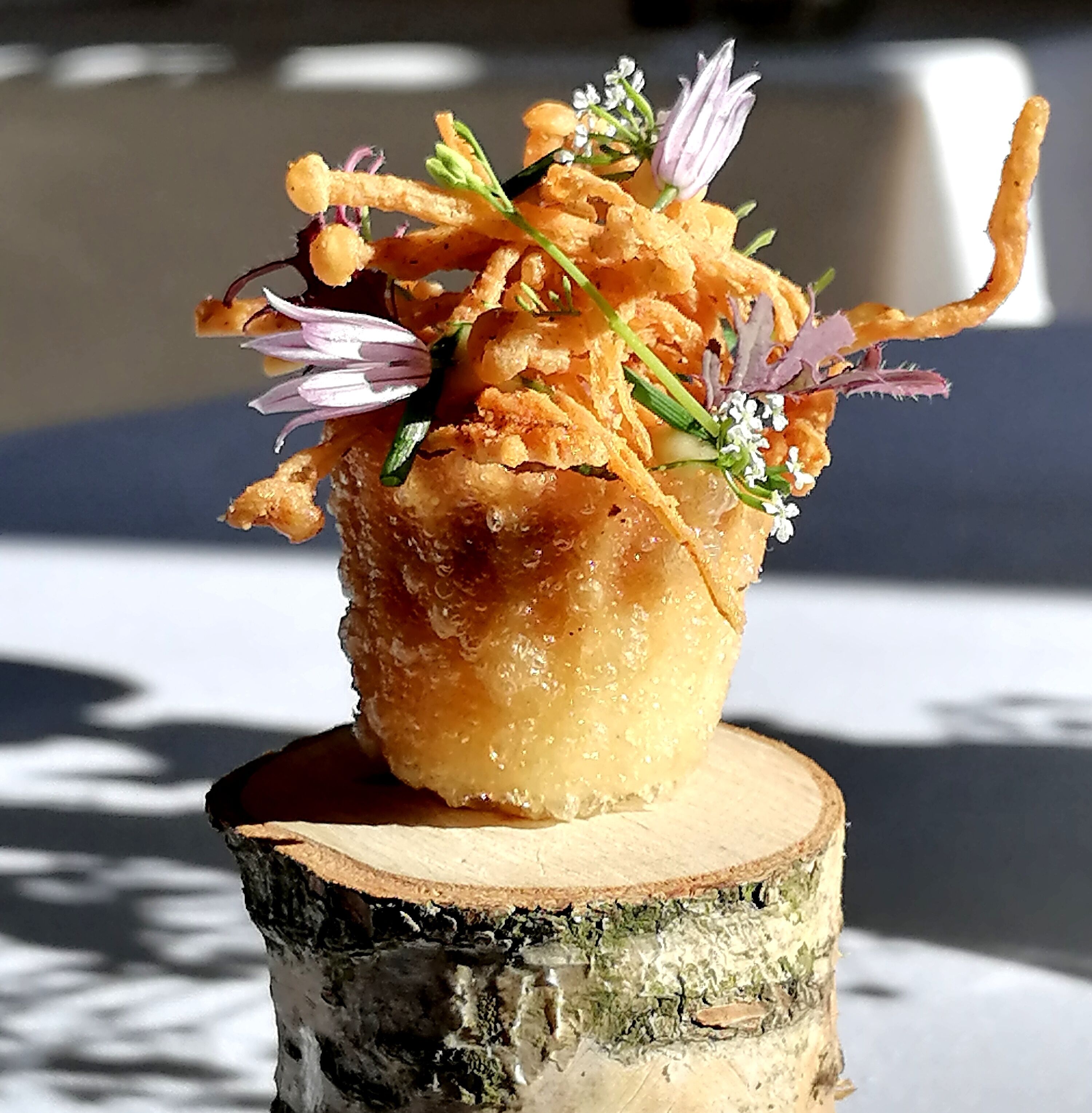 Un postre en una taza sobre una base de madera, rodeado de flores.