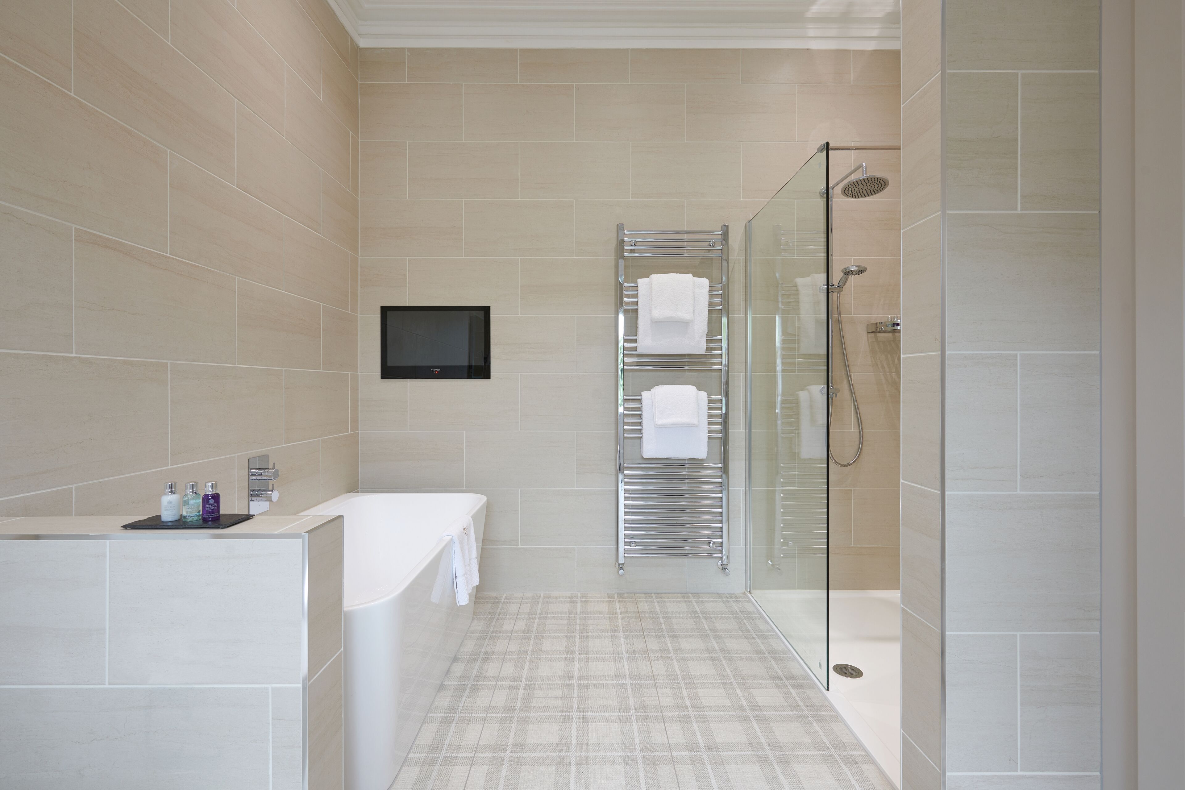 Un baño moderno con ducha de vidrio, una bañera blanca y un perchero con varias toallas.
