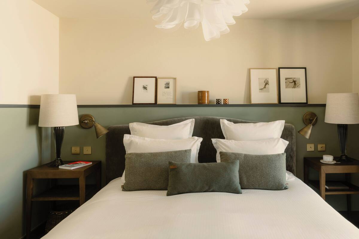 A hotel room with a bed, two bedside tables, lamps, framed pictures on the wall, and a decorative ceiling light.