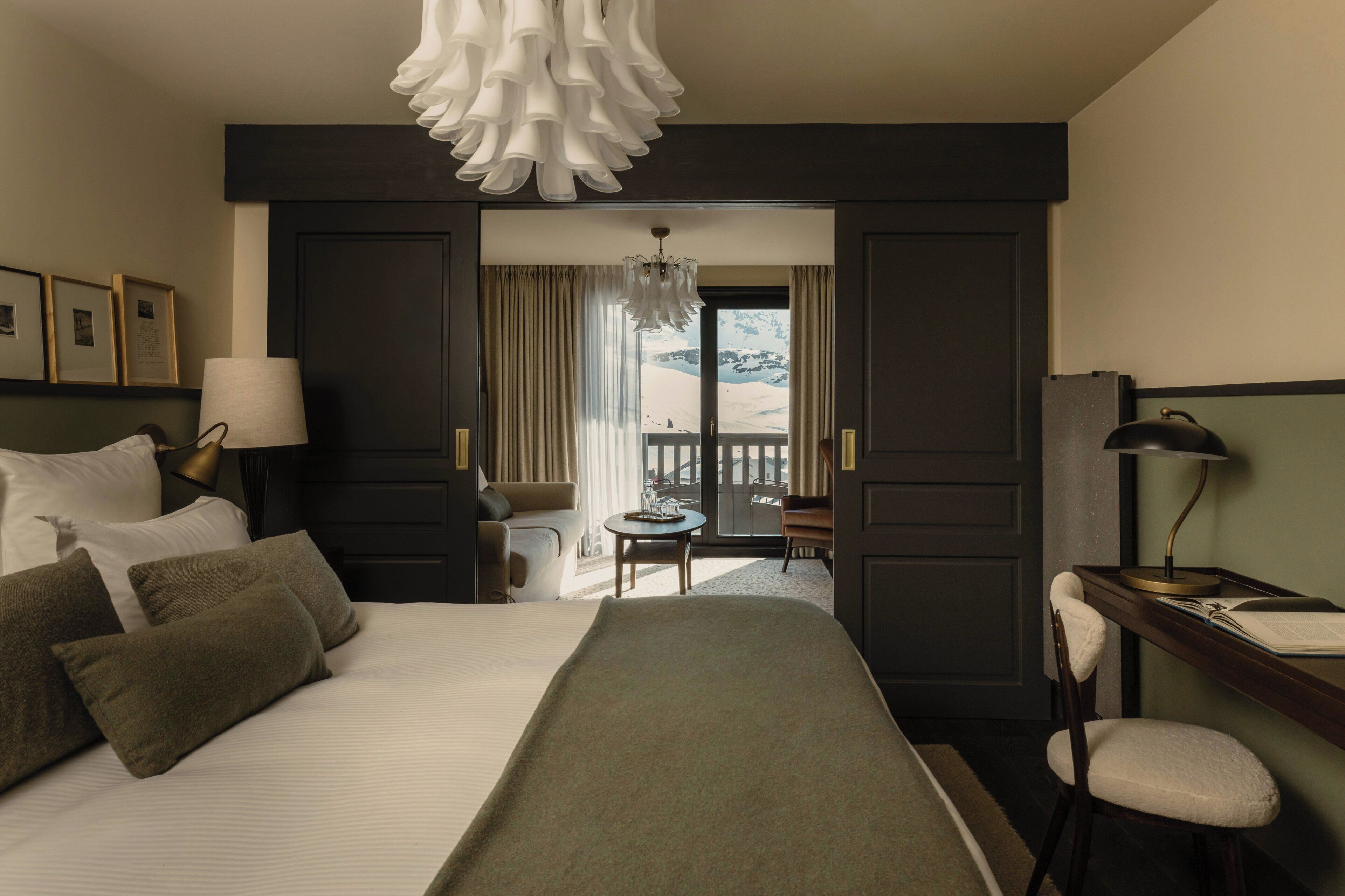 Habitación de hotel con cama, escritorio, silla, lámpara, mesa y vistas a un paisaje nevado.