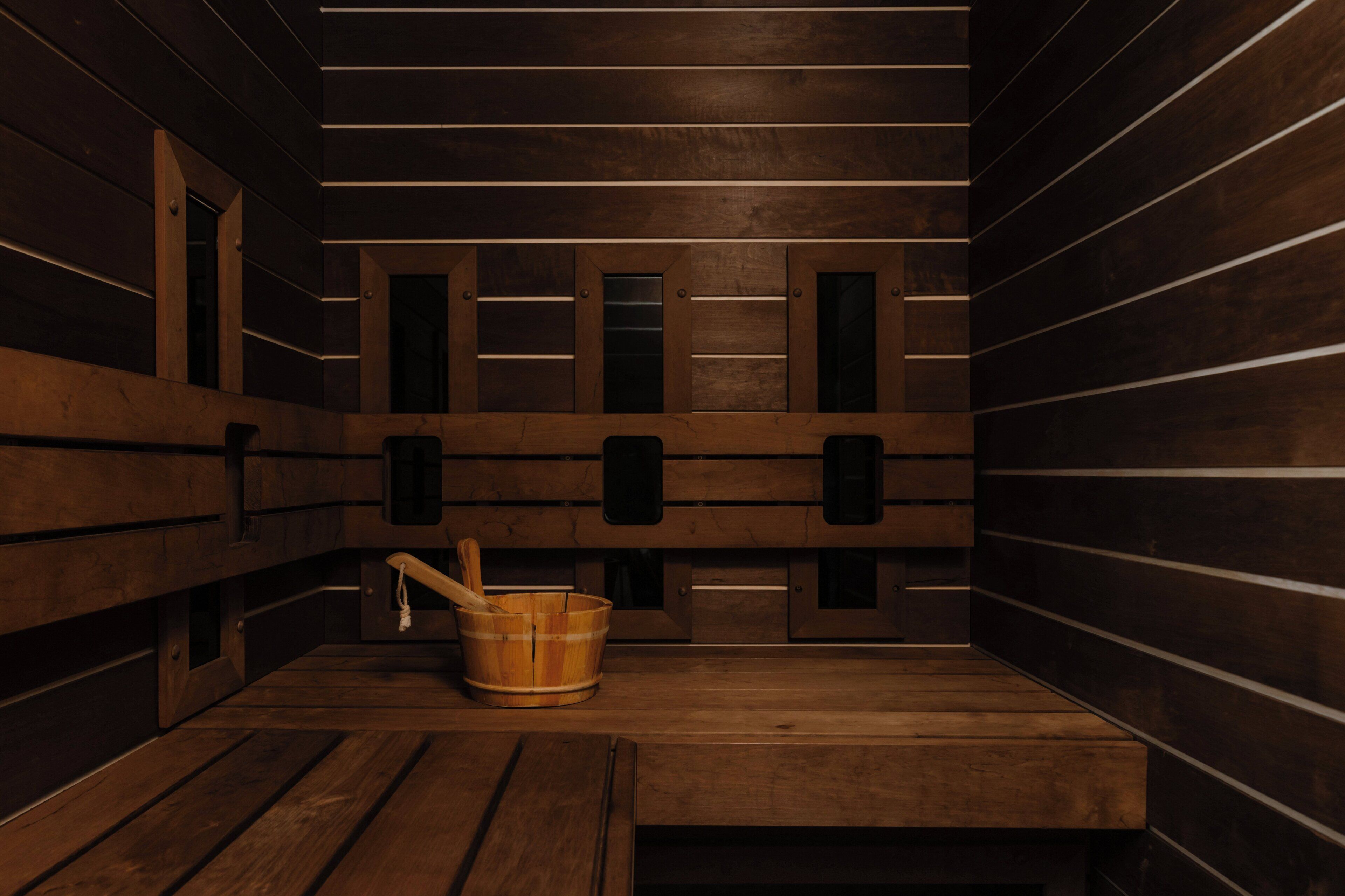 A sauna room with wooden benches, a wooden bucket, and a bench with a towel.