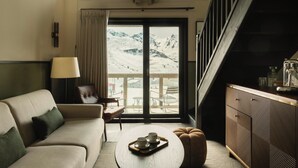 Una habitación de hotel moderna con un sofá, una mesa de centro con tazas, un armario y vistas a una montaña nevada.