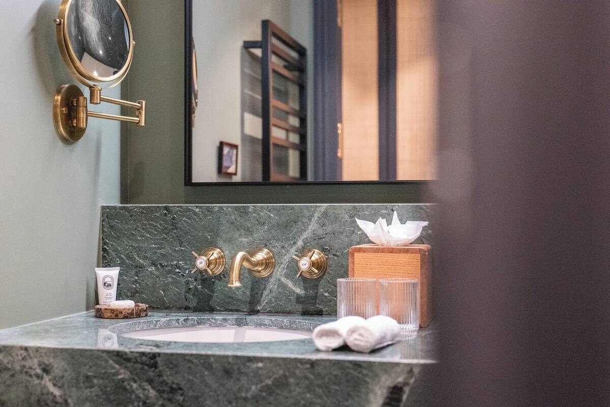 A bathroom with a marble sink, gold fixtures, a mirror, and a wooden box.