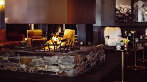 Una chimenea de piedra con sillas alrededor, un sillón cubierto de piel y una mesa con velas.