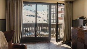 Una habitación con un ventanal grande que da a una montaña nevada, un escritorio de madera y una silla.