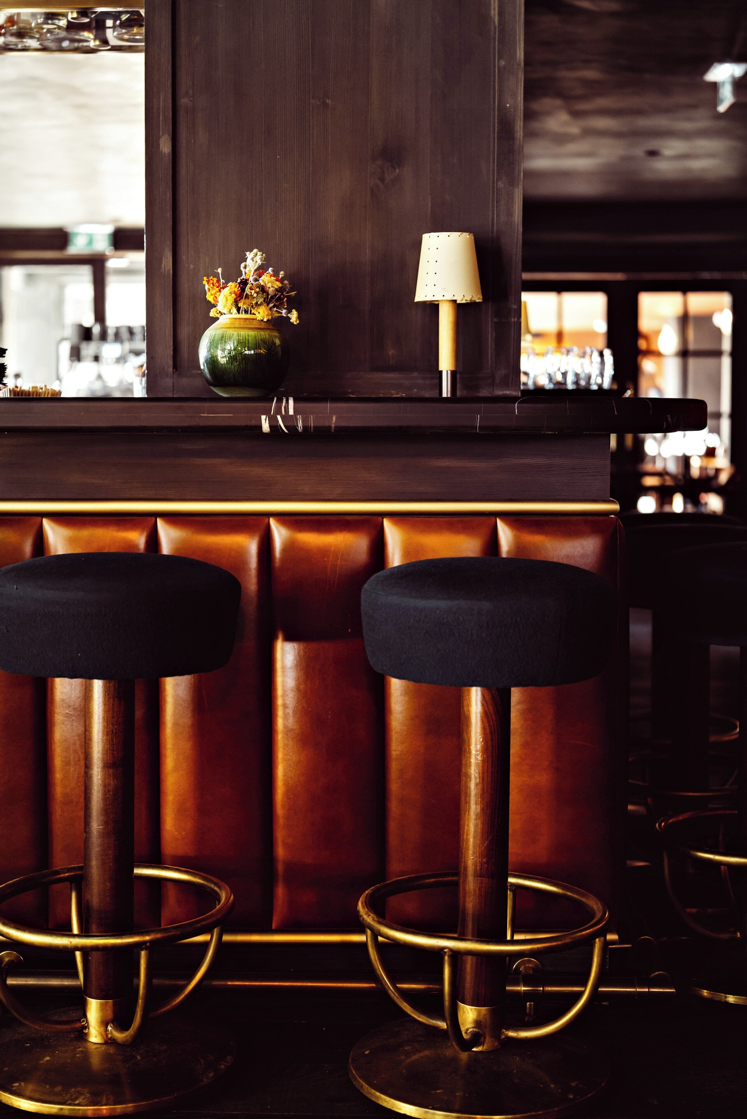 A bar area with two stools, a vase with flowers, and a lamp.