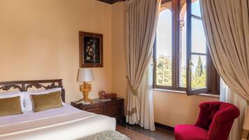 A bedroom with a bed, a nightstand, a lamp, a chair, a window with curtains, and a framed picture on the wall.