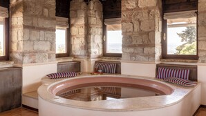 Une pièce aux murs de pierre, dotée d’une grande baignoire, de poutres en bois et offrant une vue par une fenêtre.