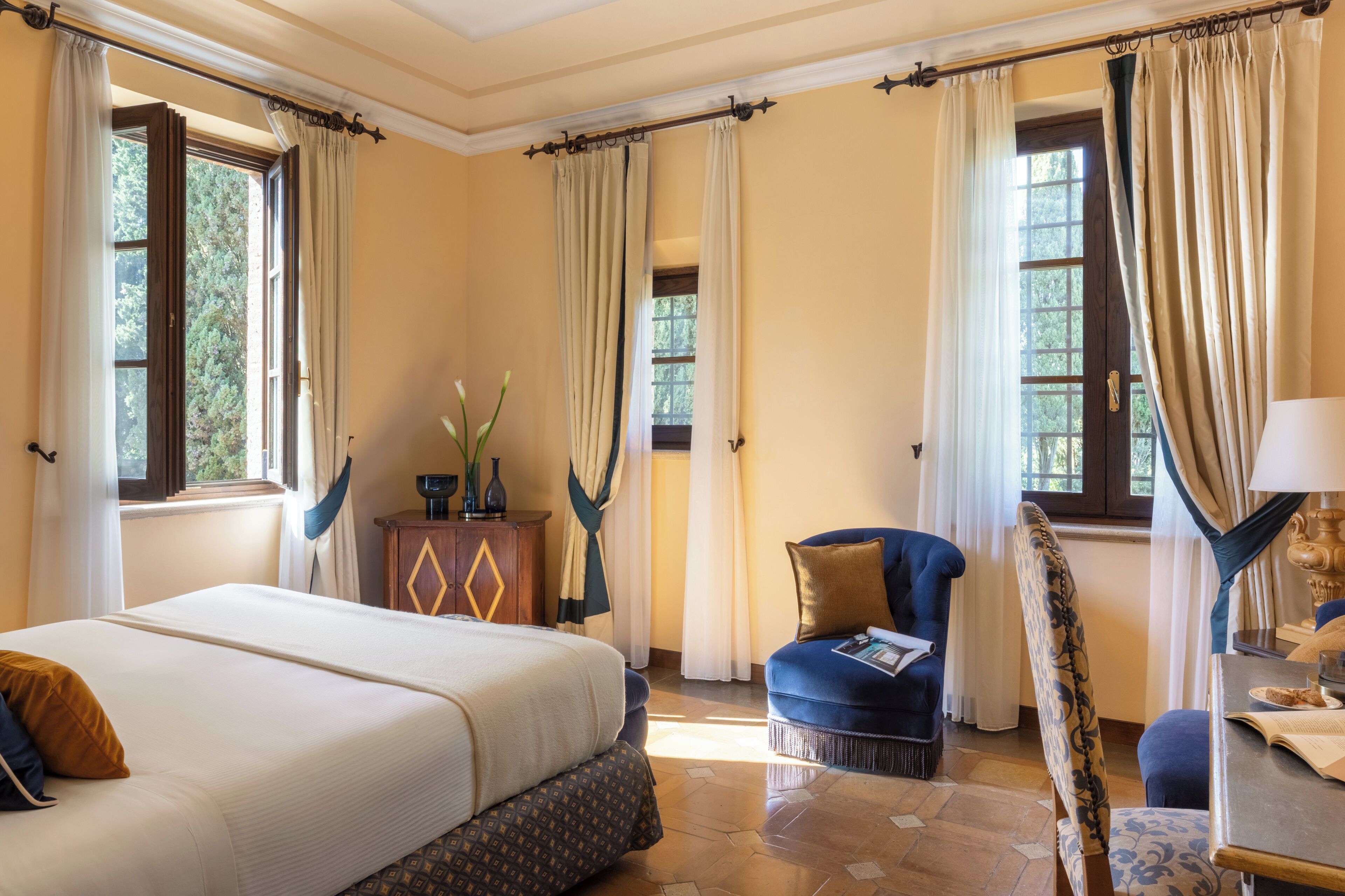 A hotel room with a large bed, a chair, a table, and curtains.