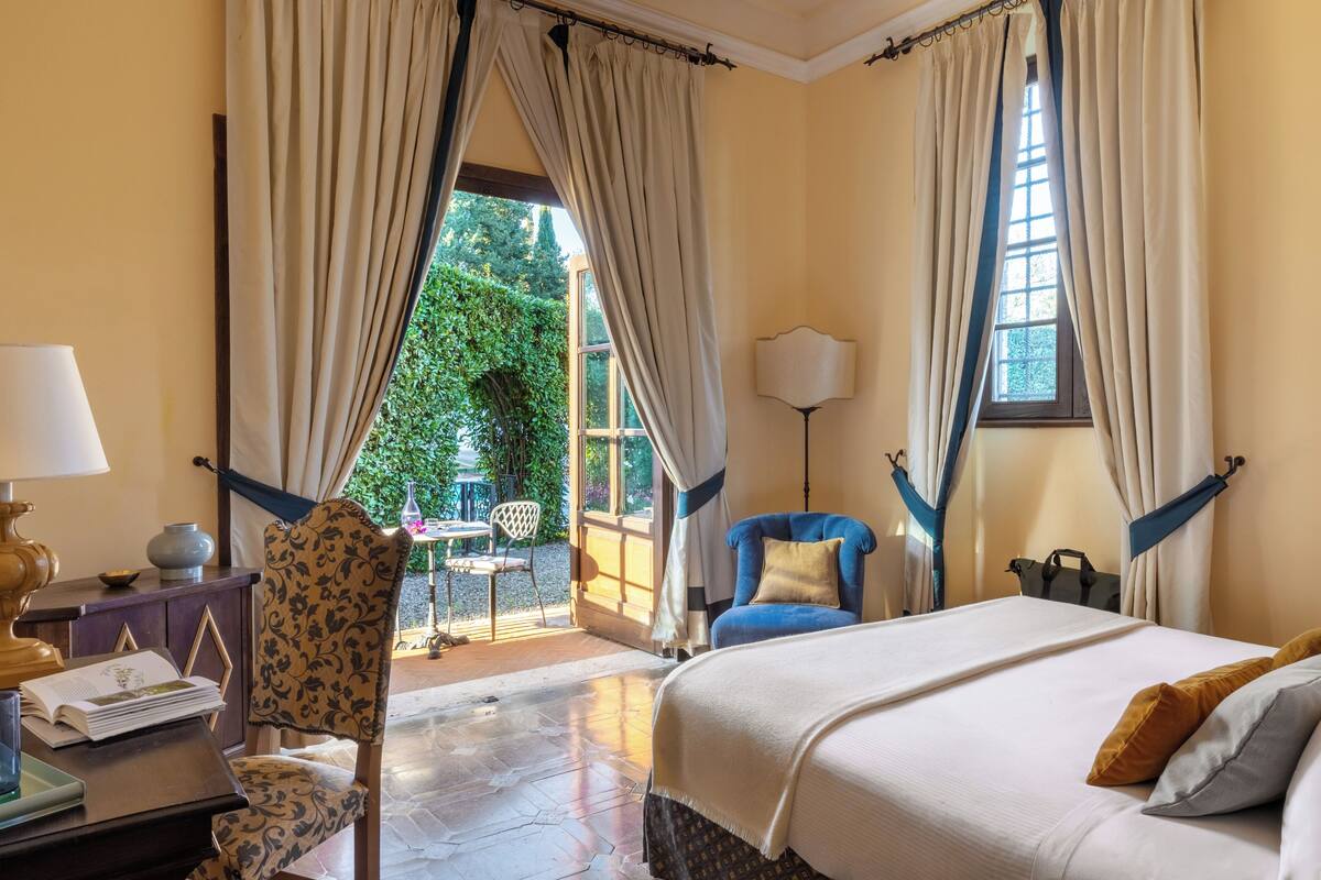 Habitación de hotel con cama, una silla, escritorio, lámpara y vistas a zonas verdes.