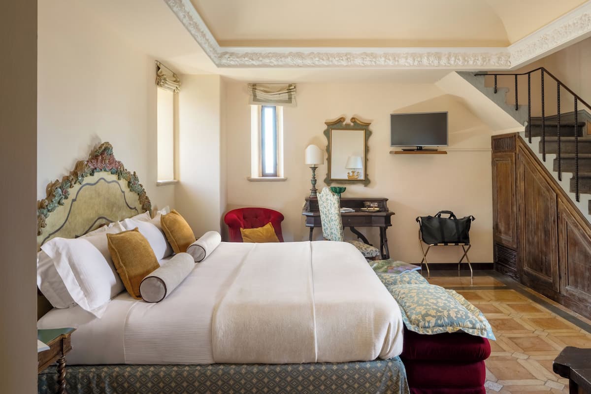 Un dormitorio con una cama grande, una silla, un escritorio, un televisor y una escalera.