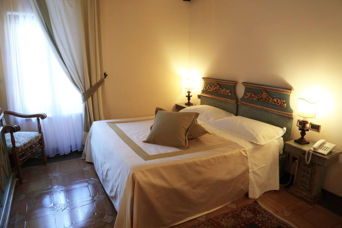 Una habitación de hotel con una cama, una mesita de noche con lámpara, una silla y un teléfono.