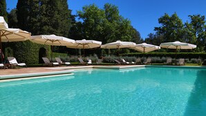 Une piscine entourée de verdure, avec des chaises longues et des parasols.