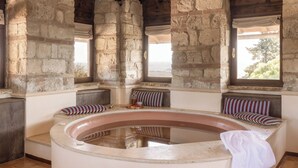 Une pièce aux murs de pierre, dotée d’un jacuzzi, de poutres en bois et offrant une vue sur l’extérieur.