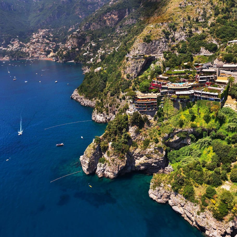 An aerial view of a coastal area with buildings on a hillside overlooking the sea.
