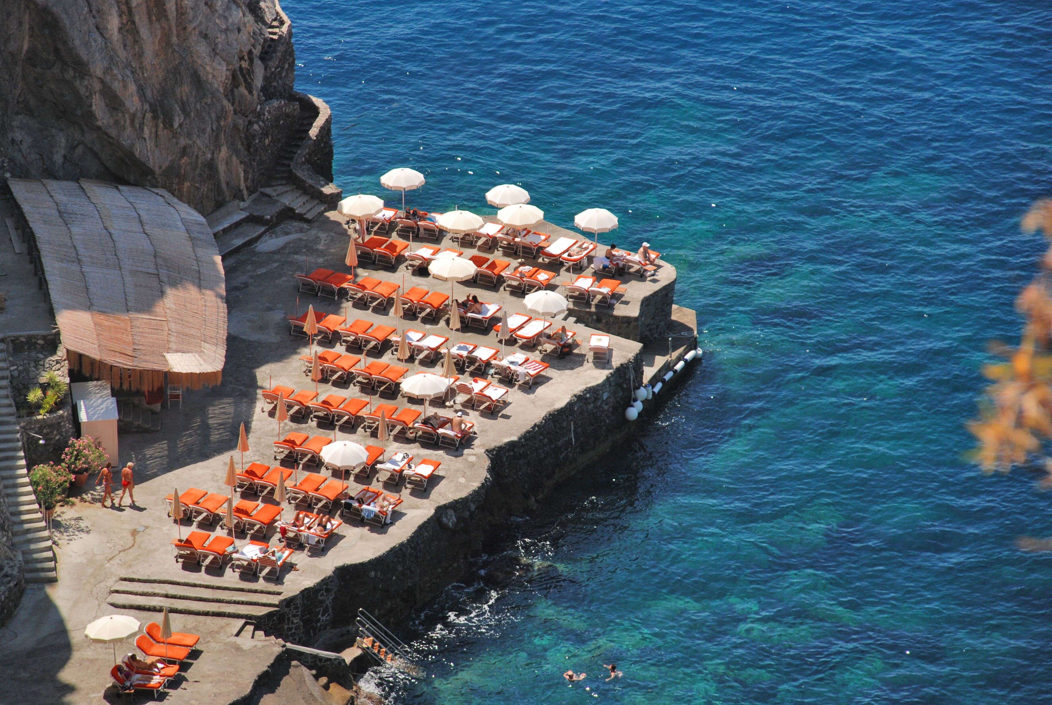A seaside terrace with rows of sun loungers and umbrellas, overlooking the ocean.