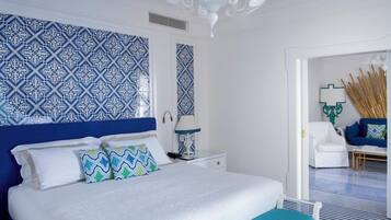 A bedroom with a large bed, white nightstands, a blue and white patterned wall, and a white chair in the corner.