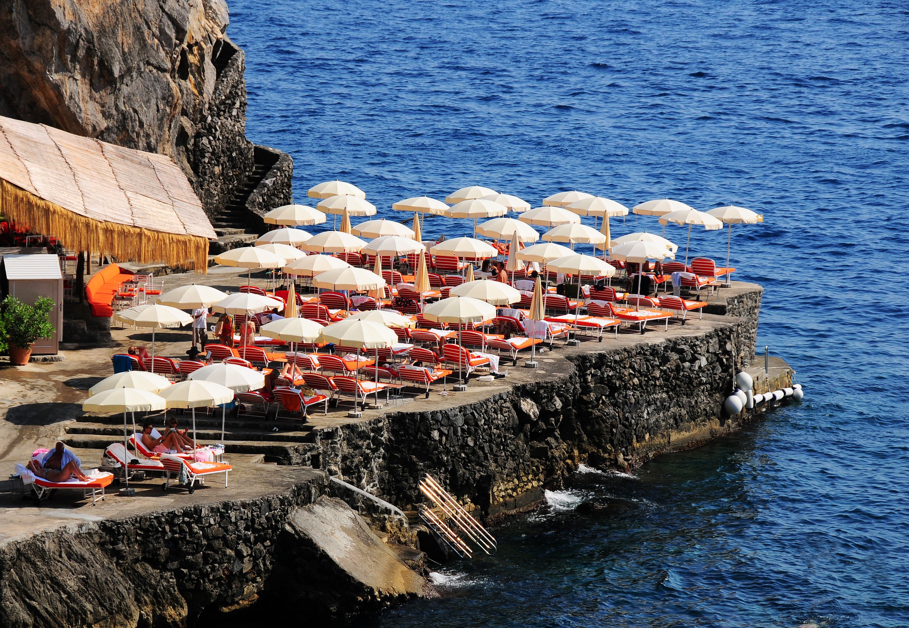 Eine Strandterrasse mit vielen Liegestühlen und Sonnenschirmen mit Blick auf den Ozean.