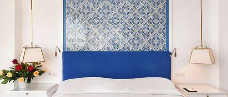 Un dormitorio ordenado con un cabecero estampado en azul, ropa de cama blanca y mesitas de noche con lámparas.
