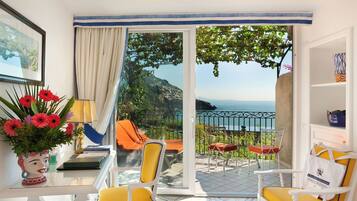 Een balkon met gele stoelen, een tafel met een bloevas en uitzicht op zee.