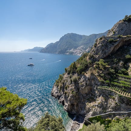 A coastal landscape with a clear view of the sea, rocky cliffs, and terraced vineyards.