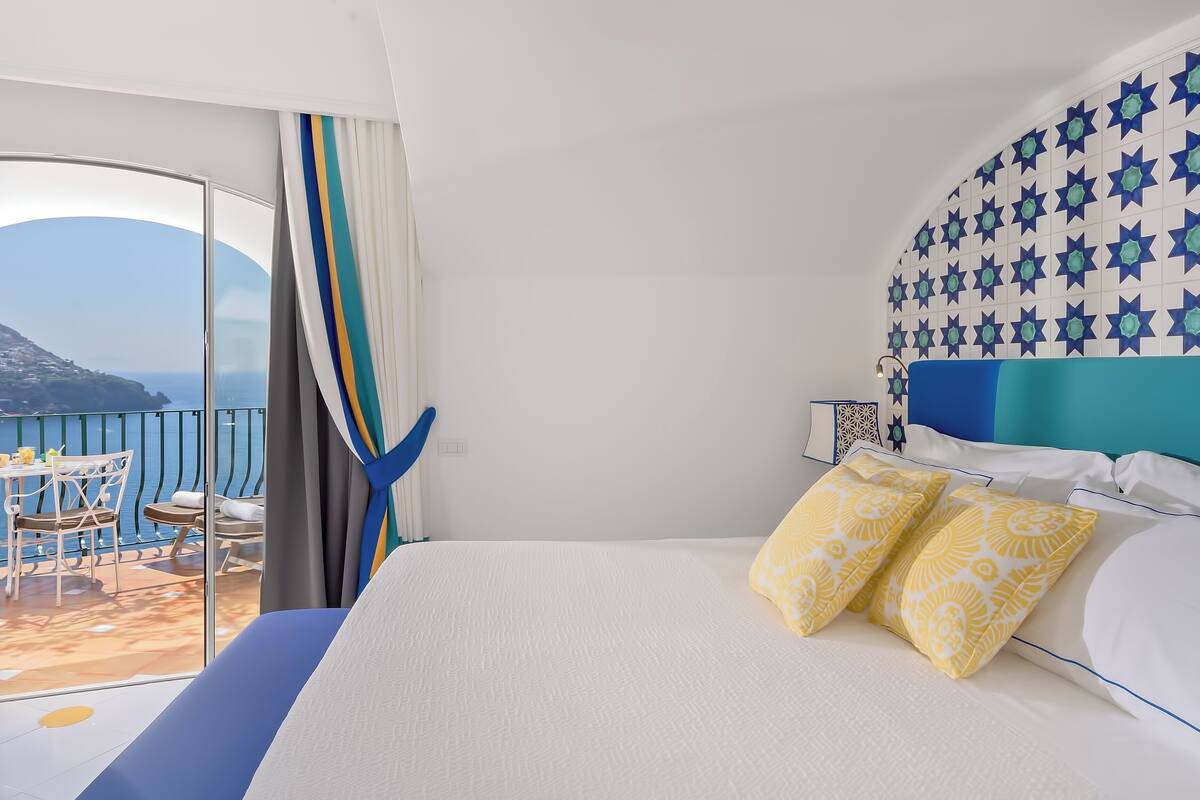 Habitación de hotel con cama, balcón con mesa y sillas, y vista al mar.