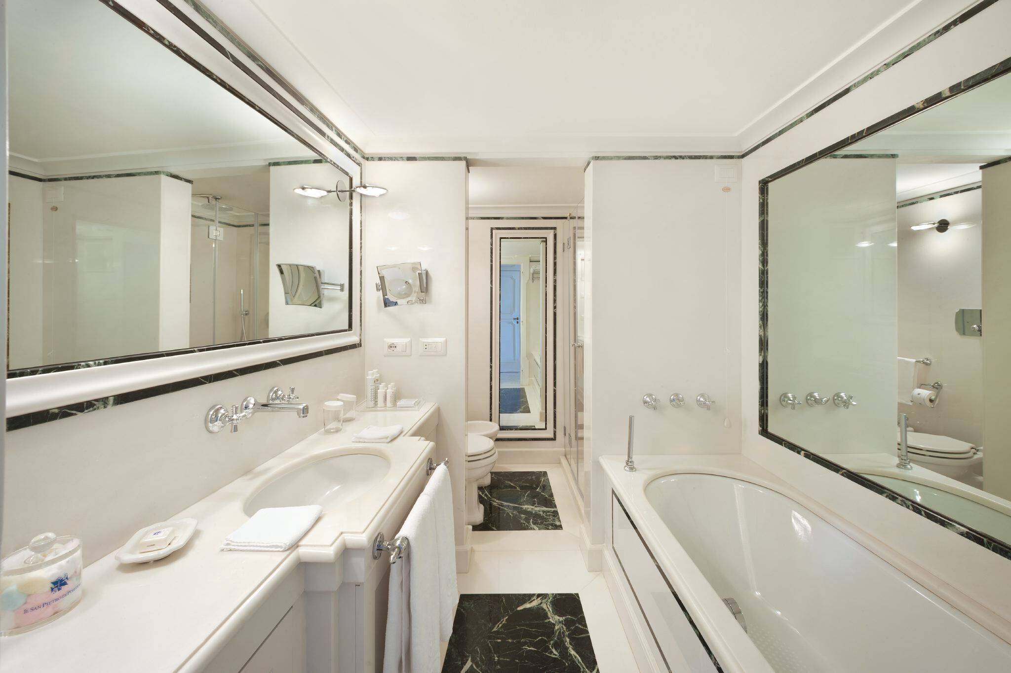 A modern bathroom with a large mirror, two sinks, a bathtub, and a toilet.