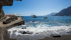 A coastal scene with a rocky shoreline, a pier with umbrellas, and boats in the water. - Il San Pietro di Positano (Positano)