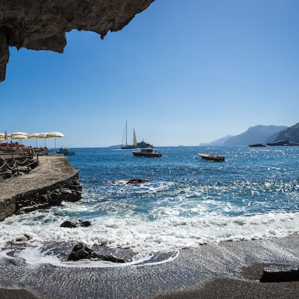 A coastal scene with a rocky shoreline, a pier with umbrellas, and boats in the water.