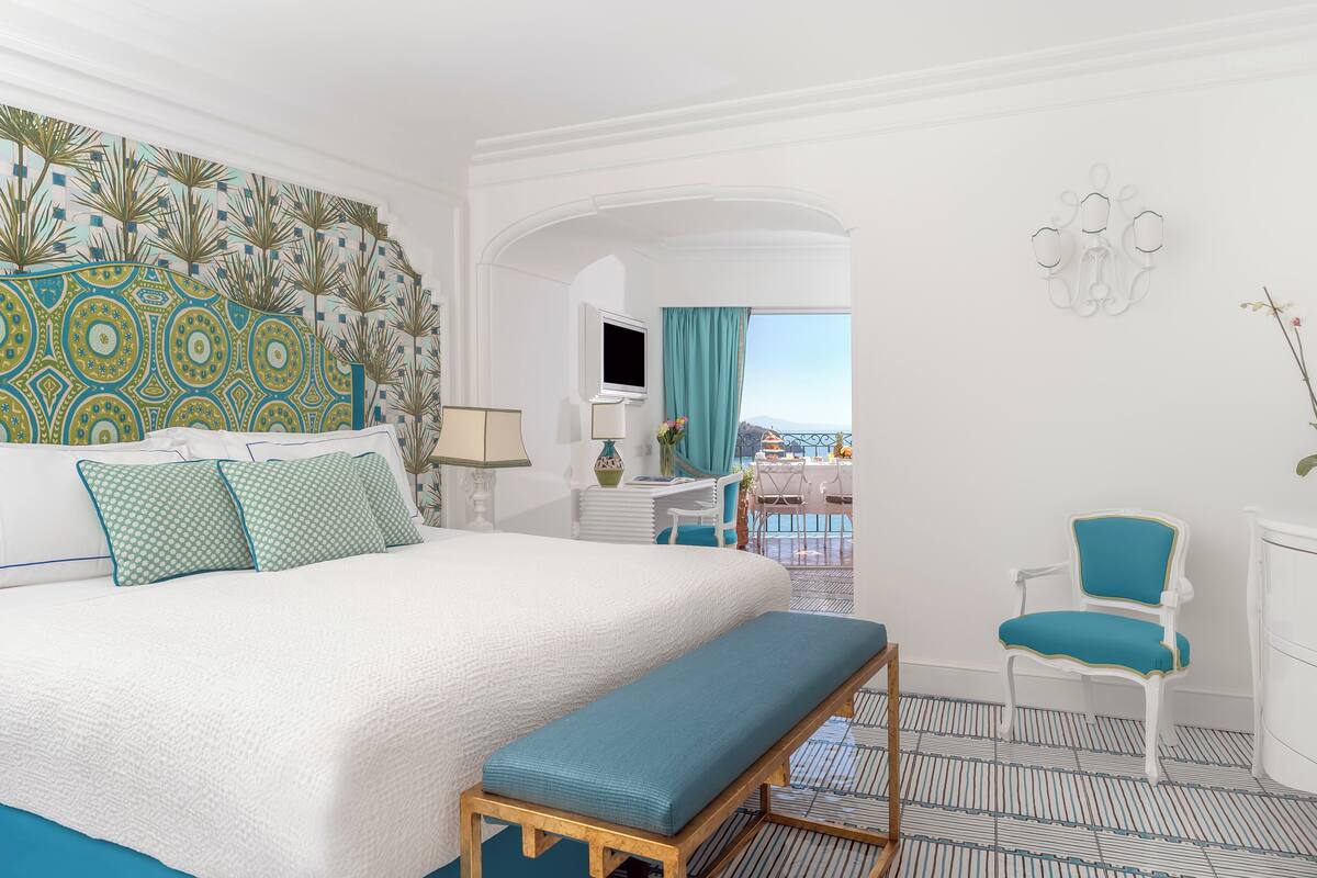 Habitación de hotel con una cama grande, una banca, un escritorio, una silla y vistas a la ciudad.