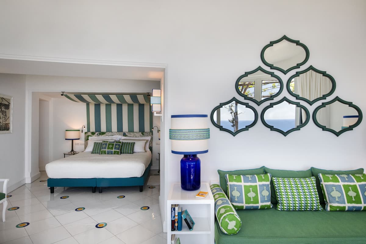 Un dormitorio con cama, mesita de noche, lámpara, estantería y espejos decorativos.