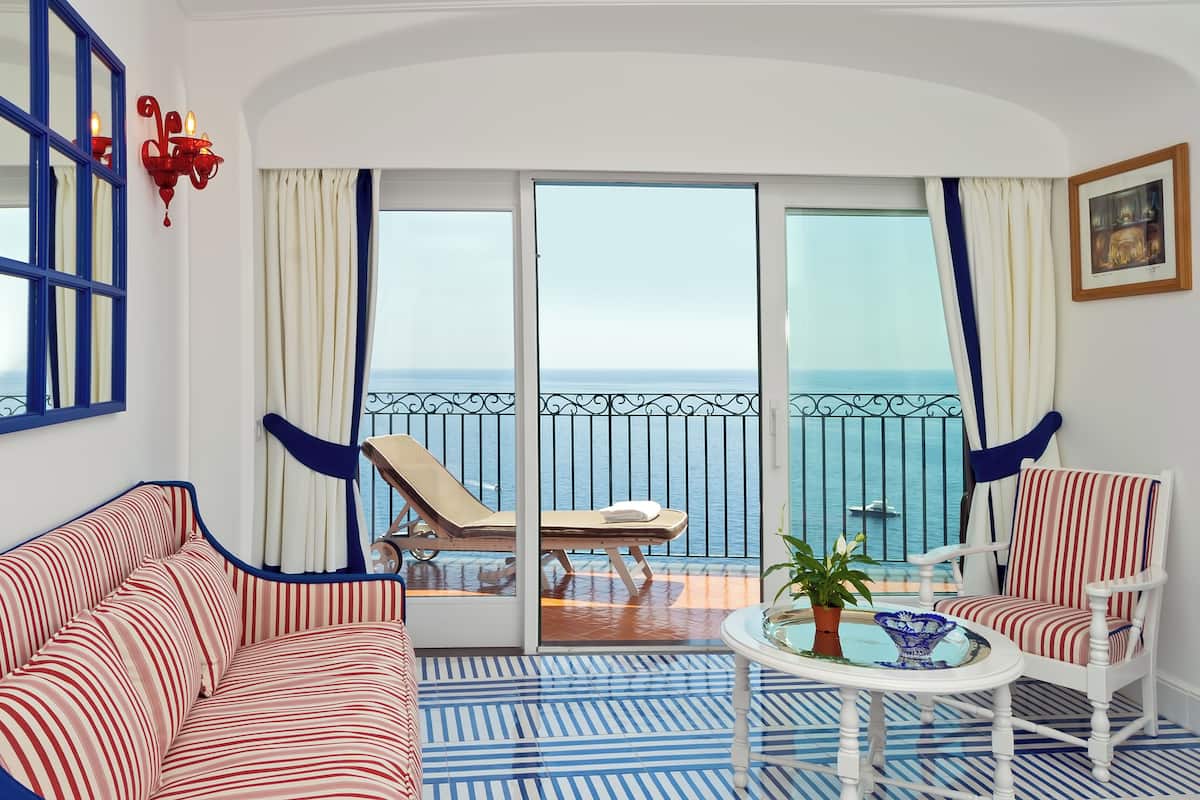Un balcón con vista al mar, un sofá a rayas, una silla y una pequeña mesa con una planta.